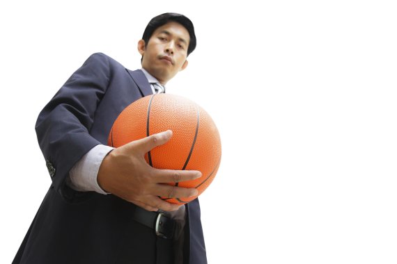 Ein asiatischer Mann mit einem Basketball in der Hand blickt hinunter zur Kamera.