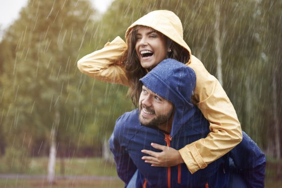 Frau in gelber Jacke hüpft im Regen auf blauen Mann
