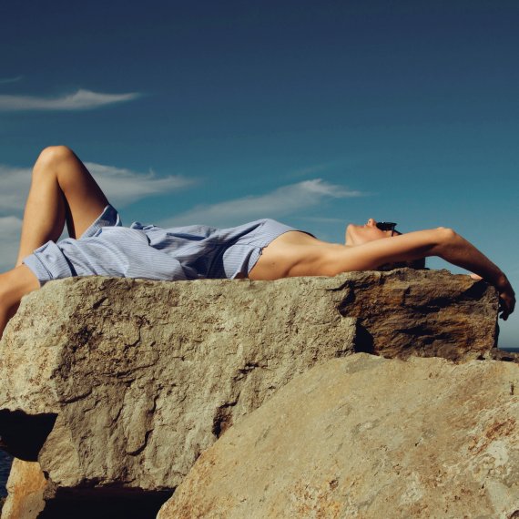 A woman sunbathing on a rocky coast.