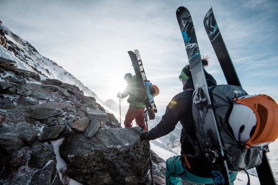 Snowboarder and skier on freeriding ascent with ABS backpack.