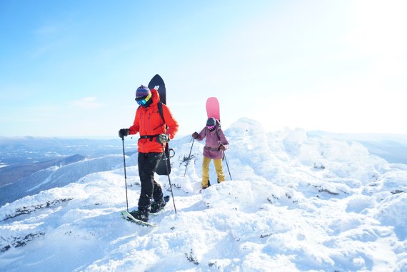 Snowboarder nutzen Schneeschuhe, um Tiefschnee-Hänge abseits der Piste zu erreichen.