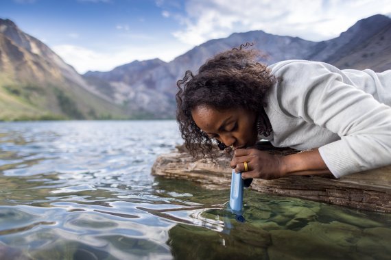 Frau trinkt aus einem Bach mit Lifestraw