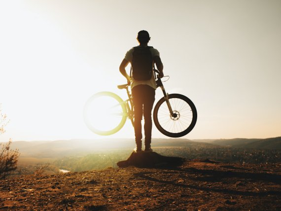 Mit dem Fahrrad umweltschonend unterwegs Biker läuft mit seinem Rad in der Hand in das Sonnenlicht