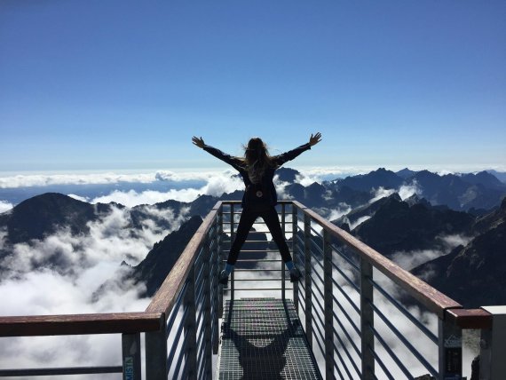 A woman stands on a viewing platform above the clouds.