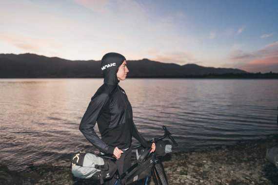 Frau mit schwarzer Jacke und Fahrrad vor See