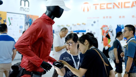 Zwei Frauen begutachten auf der ISPO Shanghai eine rote Laufjacke, die an einer Schaufensterpuppe ist. 