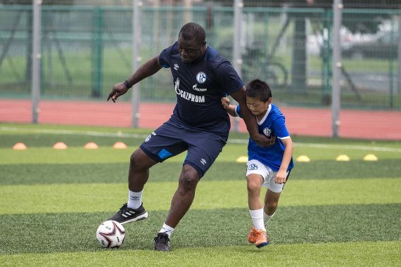 Hautnah: Gerald Asamoah, ehemaliger deutscher Nationalspieler und Manager der Schalke-U23, im Zweikampf mit einem asiatischen Jungen.