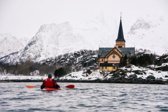 Kajakfahrer im Wasser vor einem Gebäude am beschneiten Ufer