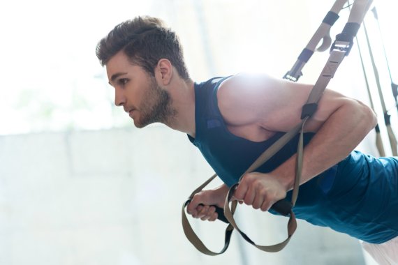 TRX Training Mann stützt sich in den Schlingentrainer während einem TRX Training