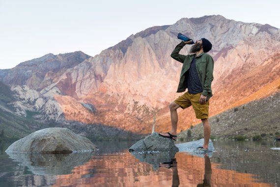 Homme buvant dans une bouteille LifeStraw devant une chaîne de montagnes