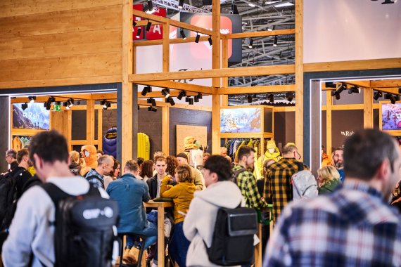 Auf der ISPO MUNICH treffen sich Textilfachhändler in einer schicken Lounge aus Holz an Tischen und unterhalten sich.
