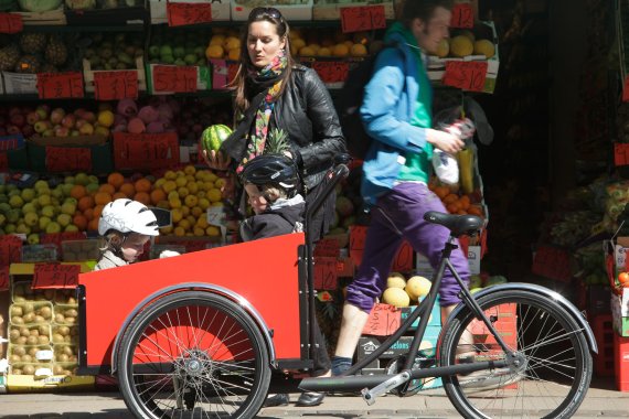 mb-151120-Lastenfahrrad_Foto Christianiabikes Mutter mit Kindern in Lastenfahrrad vor Obststand.