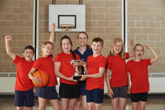 Kinder und Lehrerin bejubeln Pokal nach Basketballspiel.