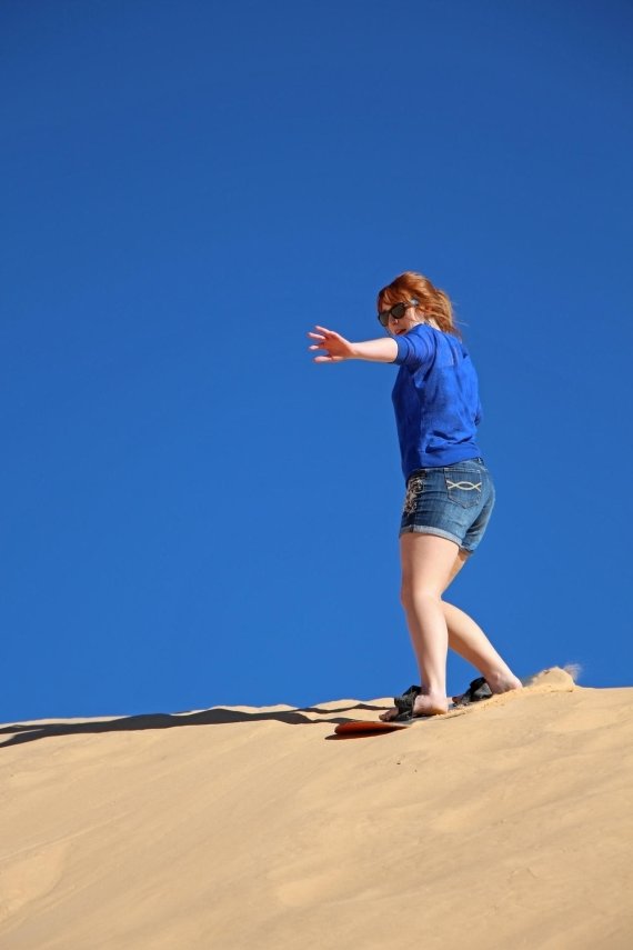 mb-151123-ThinkstockPhotos-473149248-1 Eine junge Frau surft auf einer Sanddüne.