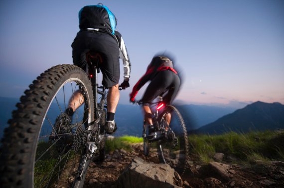 mb-pflicht-ausruestung-fuer-mountainbiker Zwei Mountainbiker in der Rückansicht, die von der Bergspitze aus runterfahren