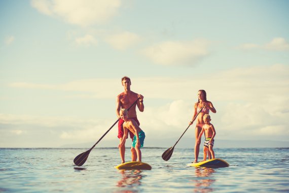 mb-Hier-lernen-Sie-Stand-Up-Paddling Mann und Frau stehpaddeln mit jeweils einem Kind