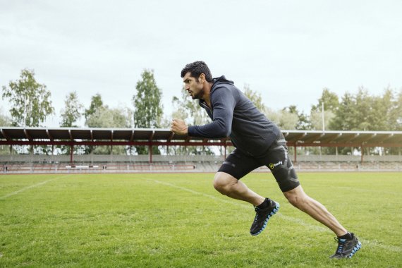mb-151127-Mbody-by-Myontech-running Mann im Sprint in Myontec-Bekleidung auf einem Sportplatz.