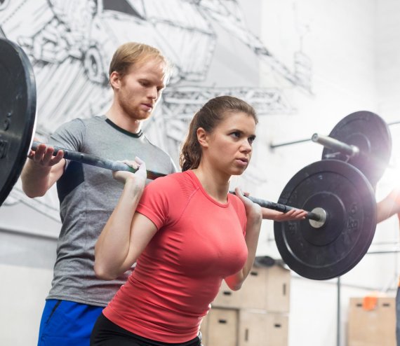 Tabata Langhanteltraining Frau macht Squads mit einer Langhantel mit ihrem Trainer