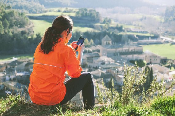 Fitness Apps Frau sitzt mit dem Handy auf einem Berg