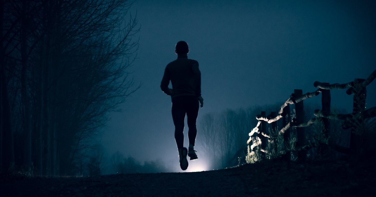 Заниматься в темноте. Ночная пробежка. Человек убегает в ночной лес. Бег с фонариком. Бегущий человек.