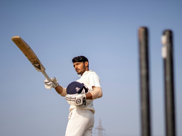 Ein indischer Cricketspieler hält Helm und Schläger.
