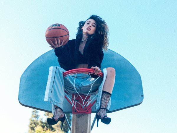 Frau sitzt im Basketballkorb und hält einen Basketball