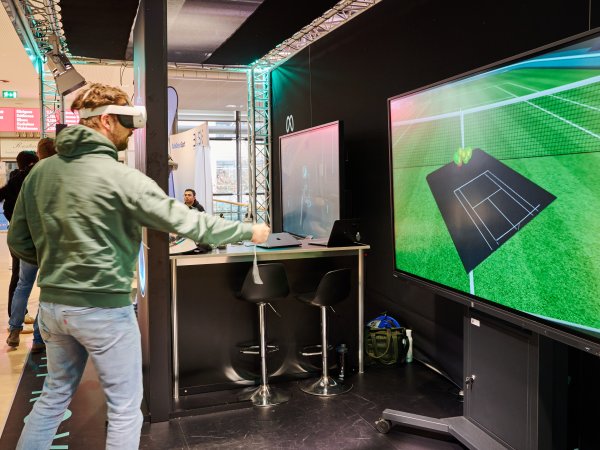 Man wears VR glasses, in the background is a screen with a playing field