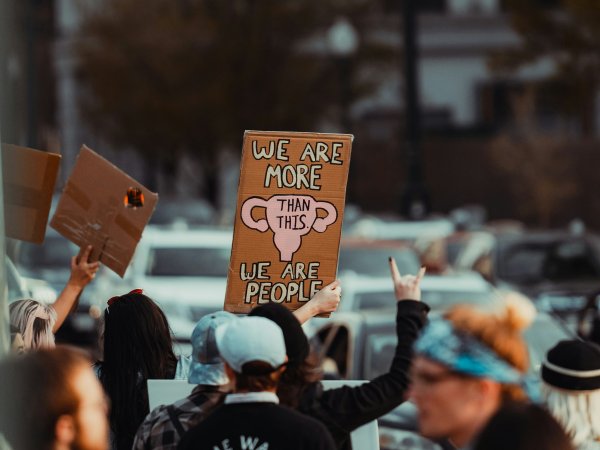 Frauen protestieren. Schild im Fokus zeigt "We are more than this - we are people"