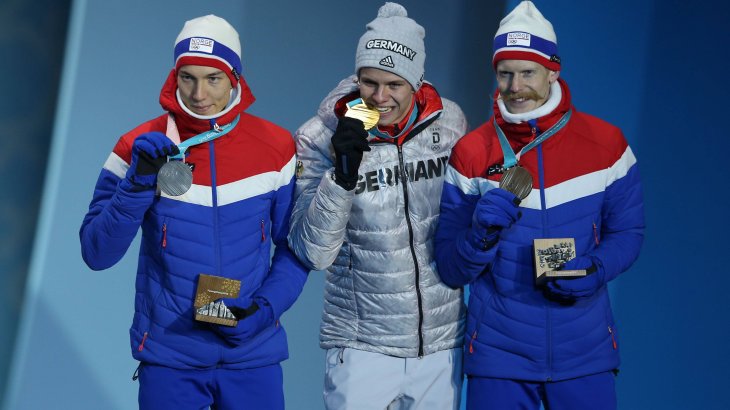 Ja, die Medaille ist echt. Andreas Wellinger, Olympiasieger im Skispringen von der Normalschanze, mit dem obligatorischen Biss in seine Goldmedaille. Mit ihm auf dem Podium die beiden Norweger Johann André Forfang und Robert Johansson 