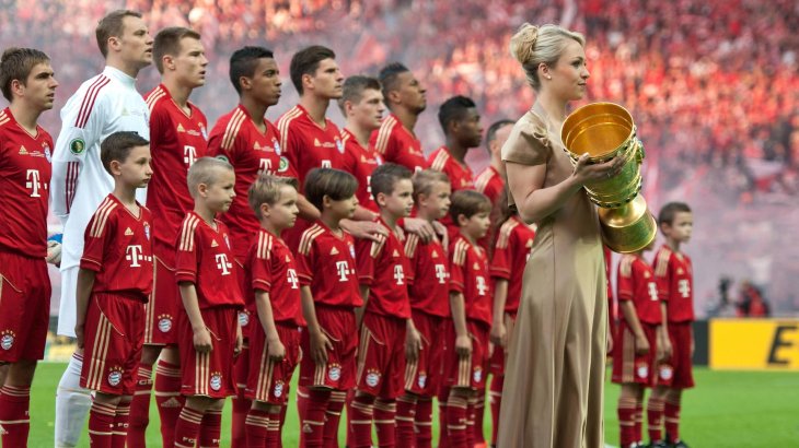 mb-151130-imago10564023h Magdalena Neuner mit dem DFB-Pokal, im Hintergrund die Mannschaft des FC Bayern.