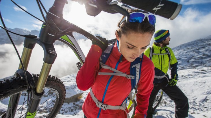mb-151130-W15_EL1Q4771_vaude_moritz_attenberger_r Zwei Mountainbiker tragen ihre Räder auf einem verschneiten Stück bergauf.