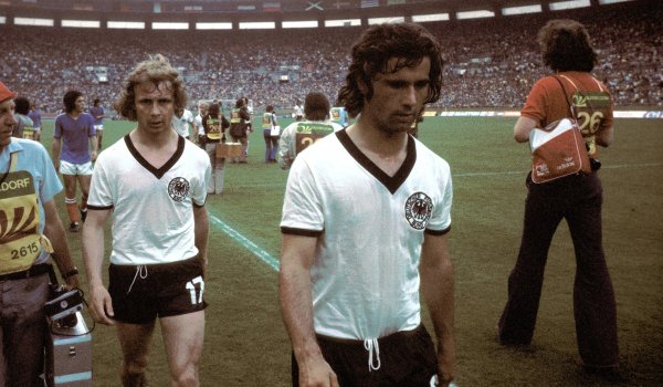 WM 1974: Ähnlich wie schon 1966 lief das DFB-Team in schlichten weißen Trikots mit V-Ausschnitt, schwarzem Kragen und schwarzen Ärmelenden auf. Im eigenen Land holten Gerd Müller (r.) und Co. in diesem Outfit den zweiten WM-Titel.