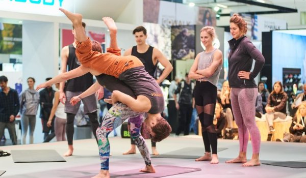 Credit: Messe München GmbH Auf der ISPO Munich 2019 wurde erstmals Kletter Yoga vorgestellt. Bei den Übungen klettert man am Partner hoch und runter während verschiedene Positionen eingenommen werden.