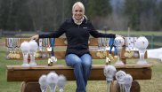 Magdalena Neuner auf einer Bank sitzend, umgeben von Pokalen und Medaillen.