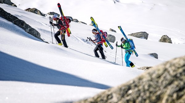 Drei Skitourengeher tragen ihre Ski am Rucksack