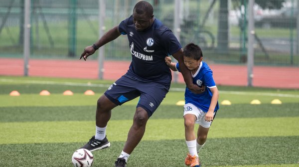 Hautnah: Gerald Asamoah, ehemaliger deutscher Nationalspieler und Manager der Schalke-U23, im Zweikampf mit einem asiatischen Jungen.