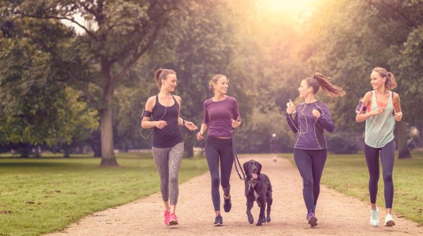Four women and a dog are jogging together in the park