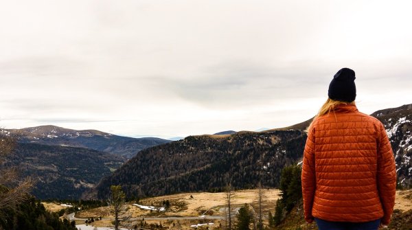 Frau mit roter Jacke blickt in die Ferne mit Bergpanorama
