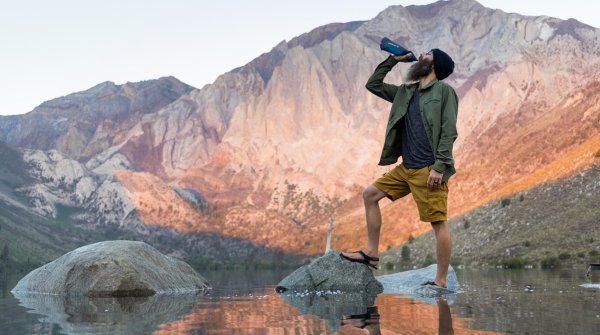 Homme buvant dans une bouteille LifeStraw devant une chaîne de montagnes
