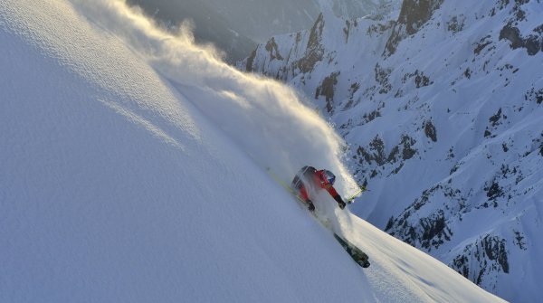 A winter sports enthusiast plows through the snow on a steep mountain slope