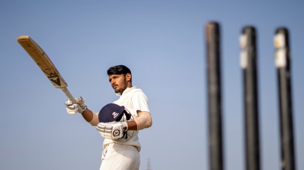 Ein indischer Cricketspieler hält Helm und Schläger.