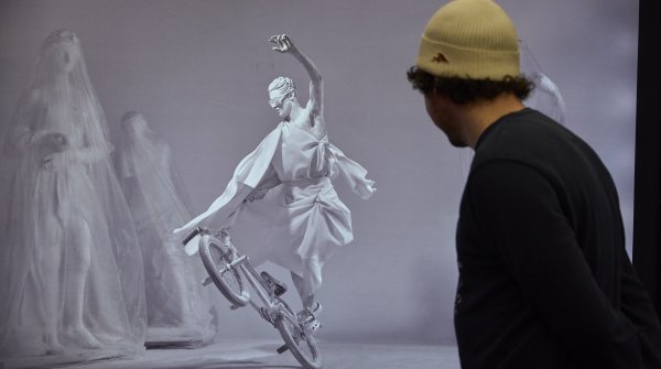 Man watching a scene in which an antique statue rides a BMX bike