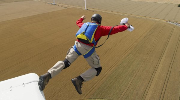 Ein Basejumper springt über einem Feld von einem Windrad.