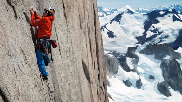 David Lama beim Klettern mit verschneitem Bergpanorama im Hintergrund.