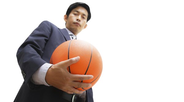 Ein asiatischer Mann mit einem Basketball in der Hand blickt hinunter zur Kamera.