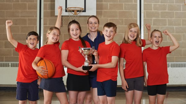 Kids and their teacher cheering after a basketball-game with a trophy.