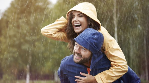 Frau in gelber Jacke hüpft im Regen auf blauen Mann