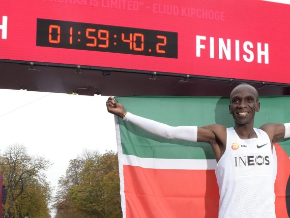 Einer der besten Marathonläufer aller Zeiten Eliud Kipchoge steht an der Ziellinie und hält stolz seine Heimatflagge in die Höhe