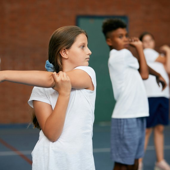 Kinder/Jugendlich wärmen sich im Sport Unterricht auf. 