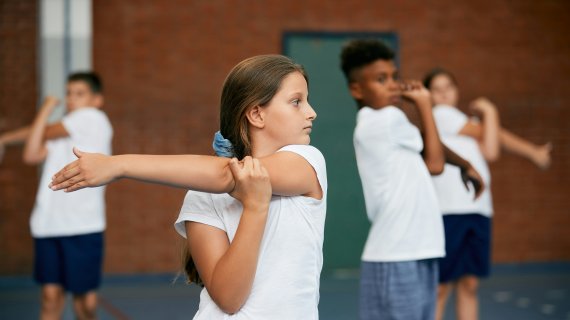 Kinder/Jugendlich wärmen sich im Sport Unterricht auf. 